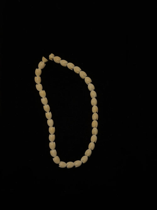 Carved bone bead necklace laid out in a frame on black velvet, IM-0142